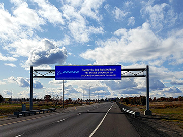 A sign above the highway leaving the Spokane International Airport, with a thank you message that reads "thank you for the generous 787 engine donation to Spokane Community College!"