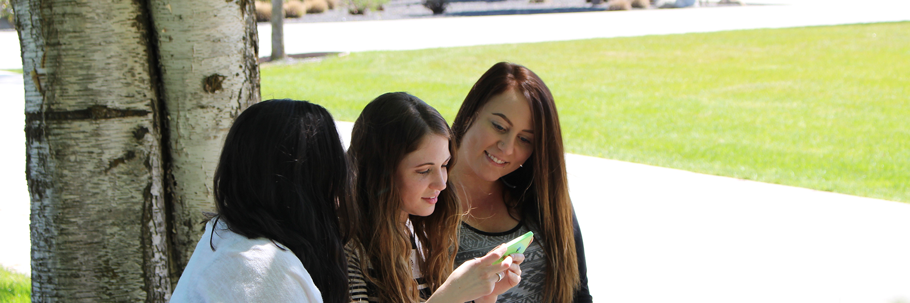 Three students sitting outside looking at a cell phone