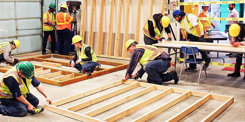 A group of carpenters, some of them apprentices, working on building a house as they sit inside and toil away on tools.