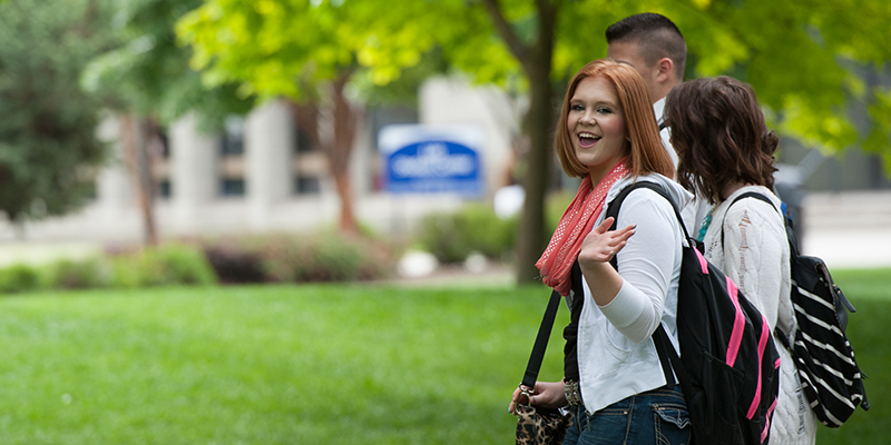 Students walking across campus waving at the camera
