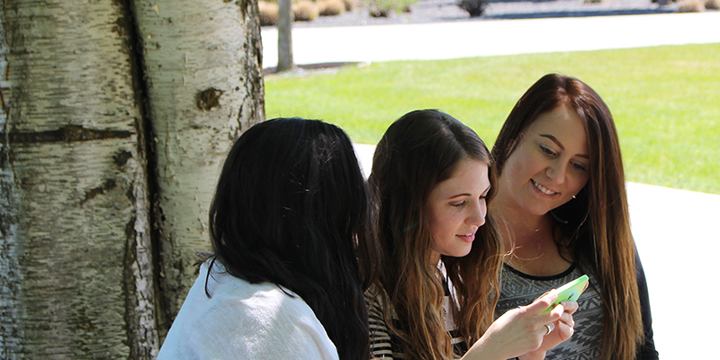 Three students sitting outside looking at a cell phone