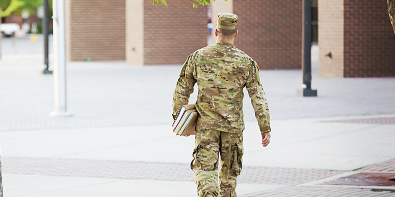 Man in uniform walking on campus with books under his arm