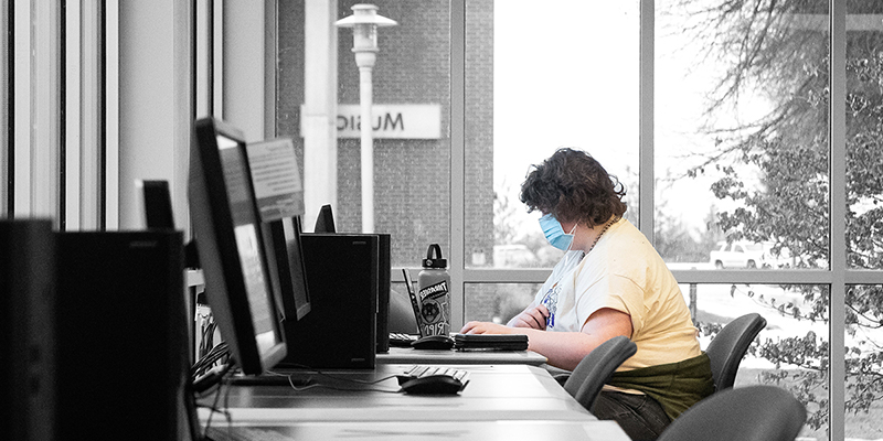 An SFCC student seated, looking at a computer in a computer lab