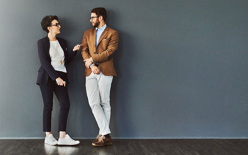 Shot of two designers having a conversation while leaning against a wall