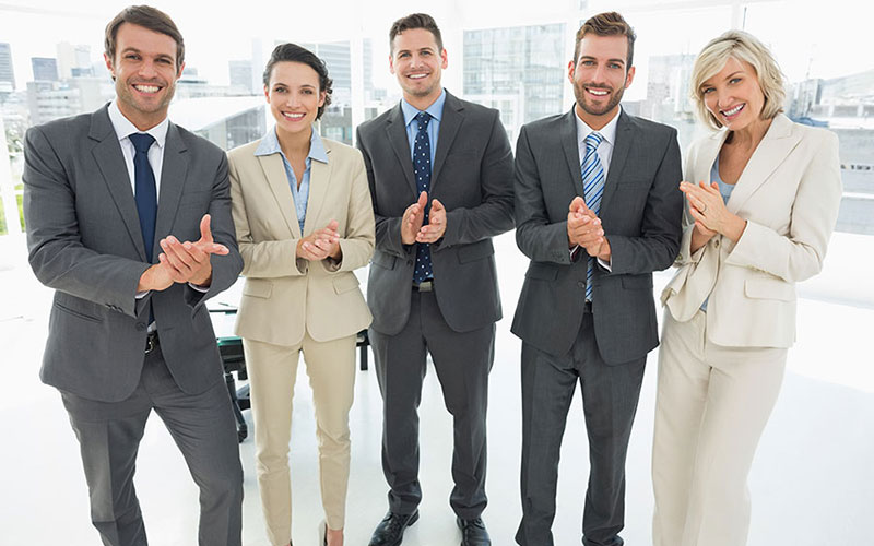 Portrait of a confident business team clapping hands together in a bright office.