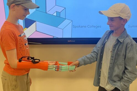 A student shaking hands with another student wearing a mechanical arm.