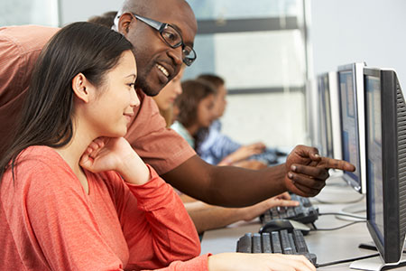 students in a computer lab, receiving help from an instructor