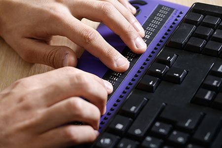 Hands typing on a braille keyboard.