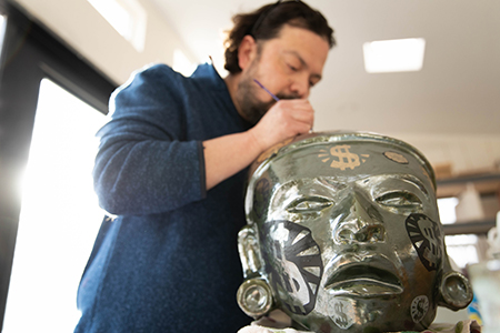 Artist Horacio Rodriguez working on sculpture of a human face.
