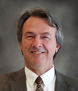 Jim Brady staring forward at the camera in front of a gray background